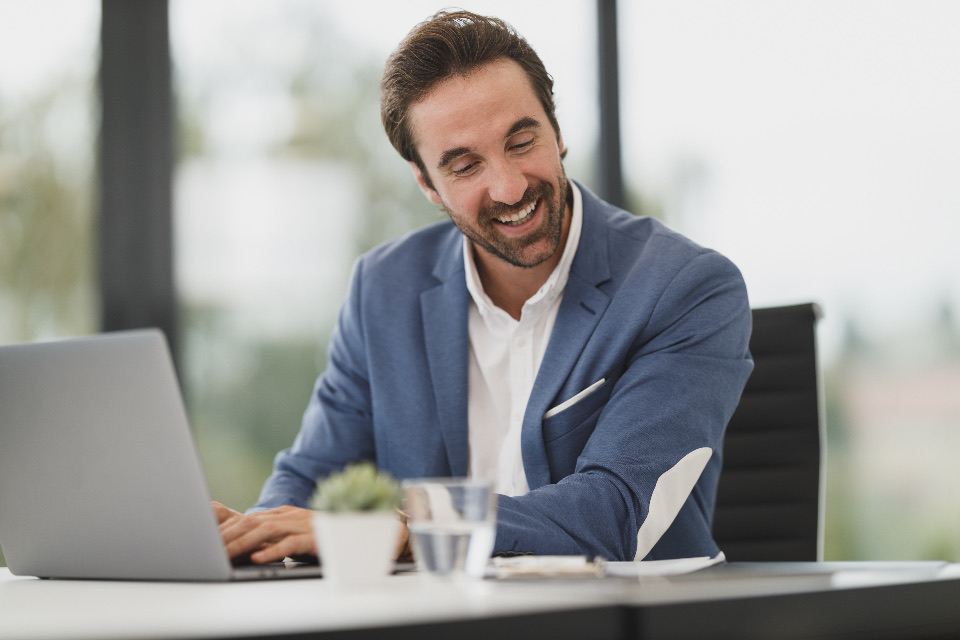 A smiling professional in a blazer working on a laptop