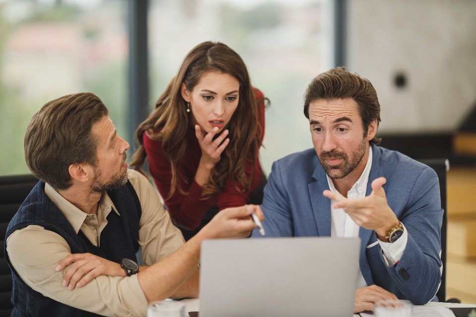 Three colleagues reviewing a laptop together in a business meeting