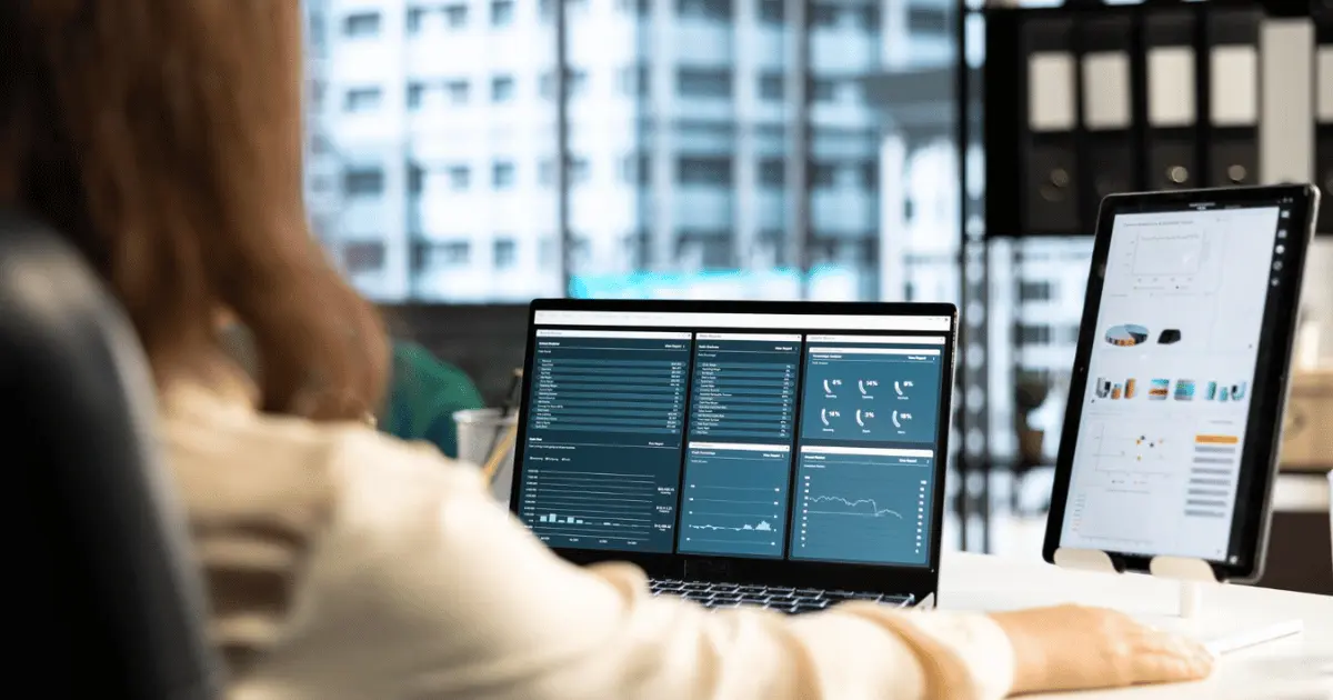 Person reviewing dashboard reports on a laptop and tablet at a desk