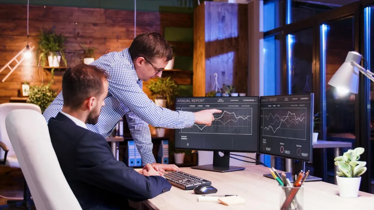 Two colleagues reviewing performance and analytics dashboards on dual monitors in an office